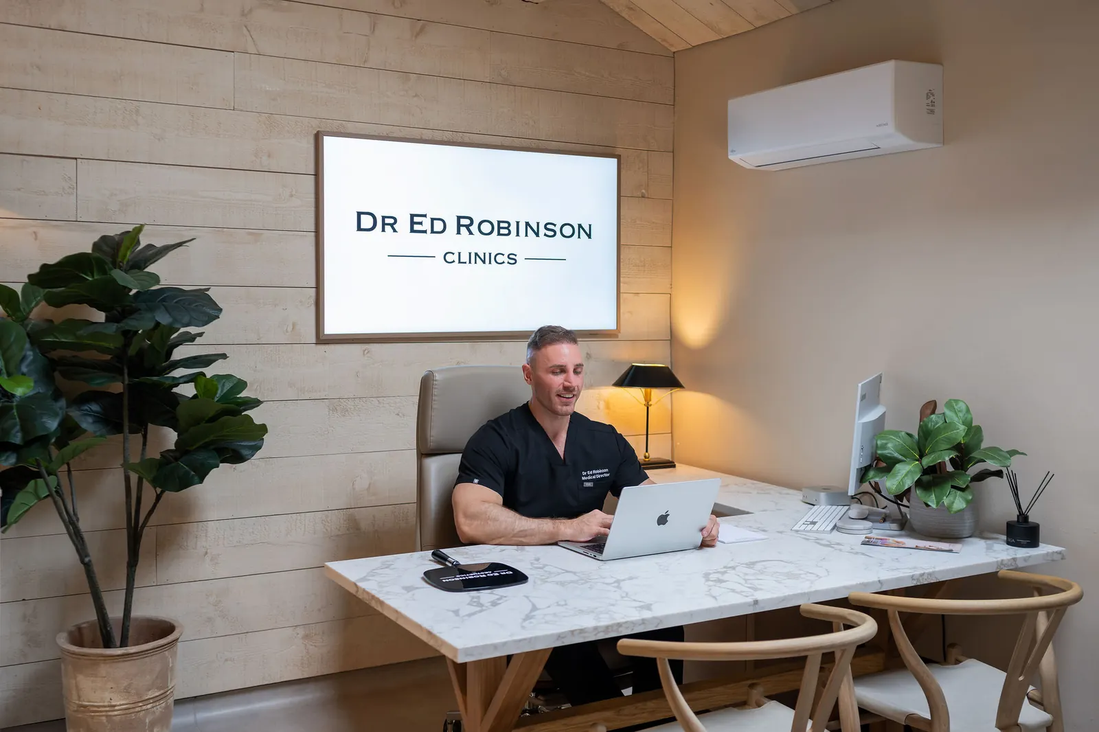 Dr Ed Robinson at his desk in the consultation room beneath the Dr Ed Robinson Clinics sign